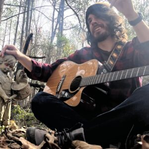 person sitting in forest holding guitar